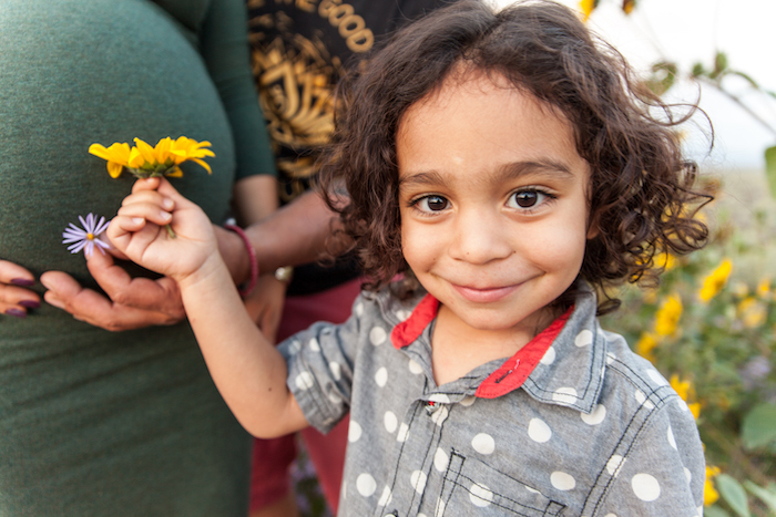 Young boy holding yellow flower standing in front of pregnant mother