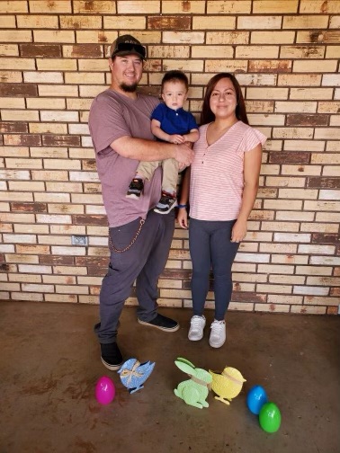 Mother and father with little boy standing in front of a brick wall with toys at their feet