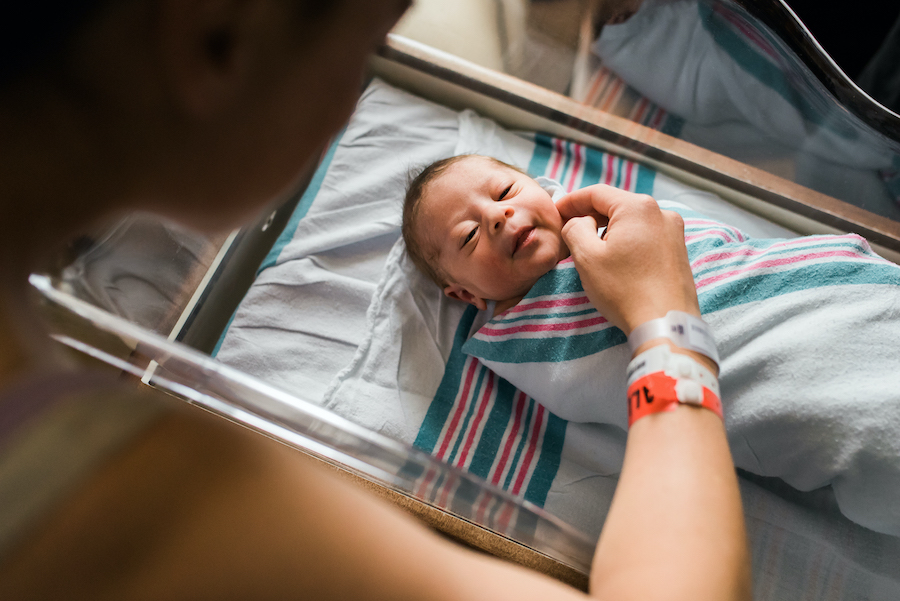 Mother touching swaddled new born baby in bassinet