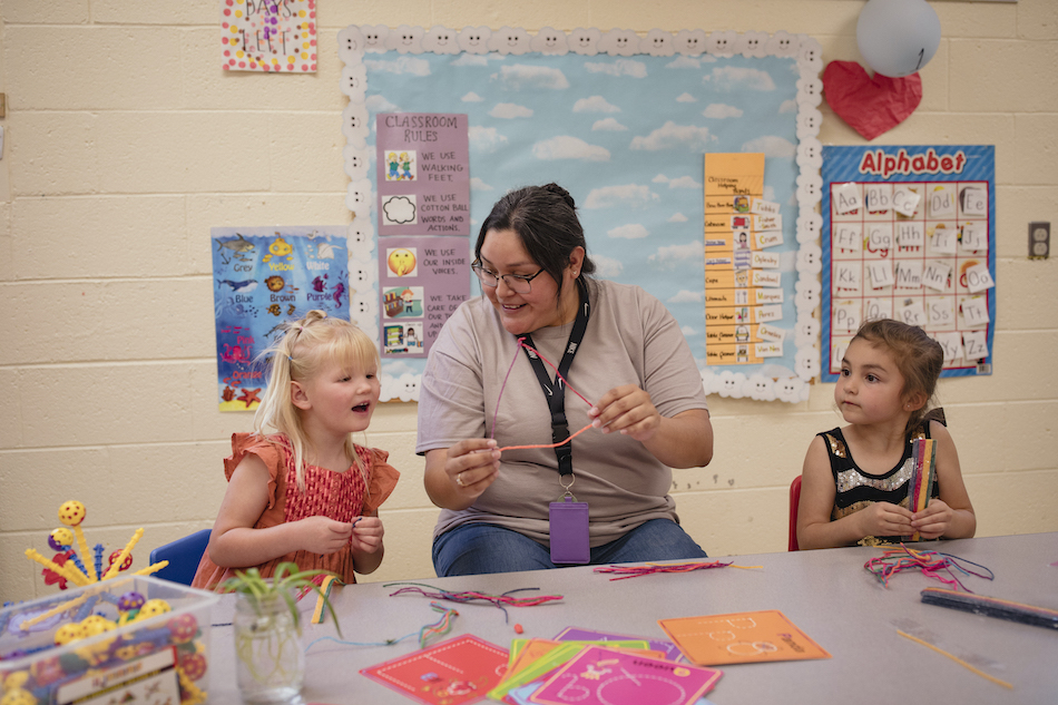 Preschool teacher making art crafts with two children at classroom table
