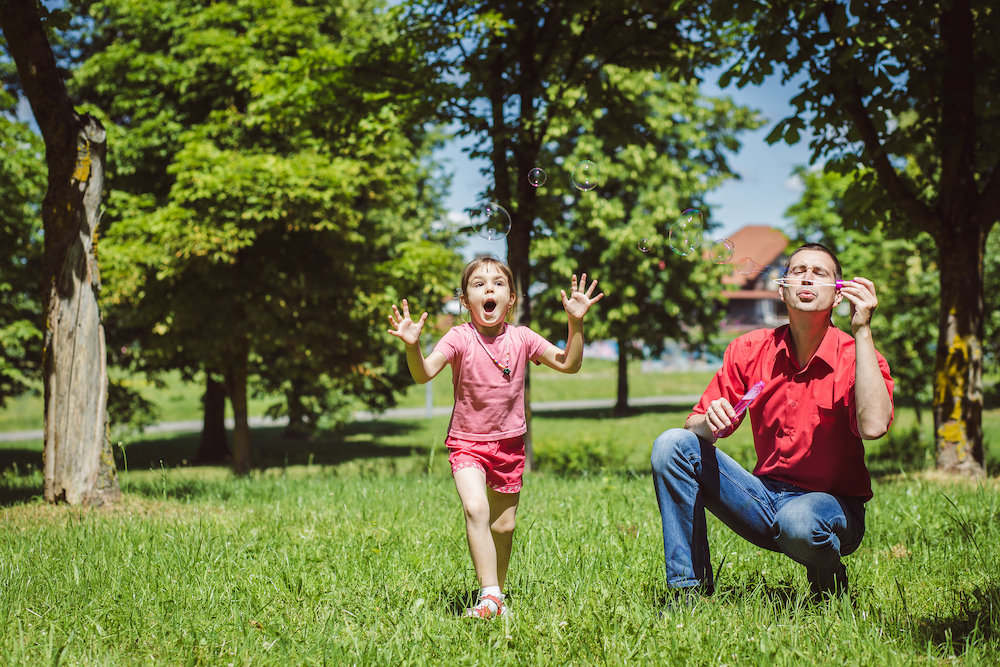 A dad and his daughter are making bubbles in the park