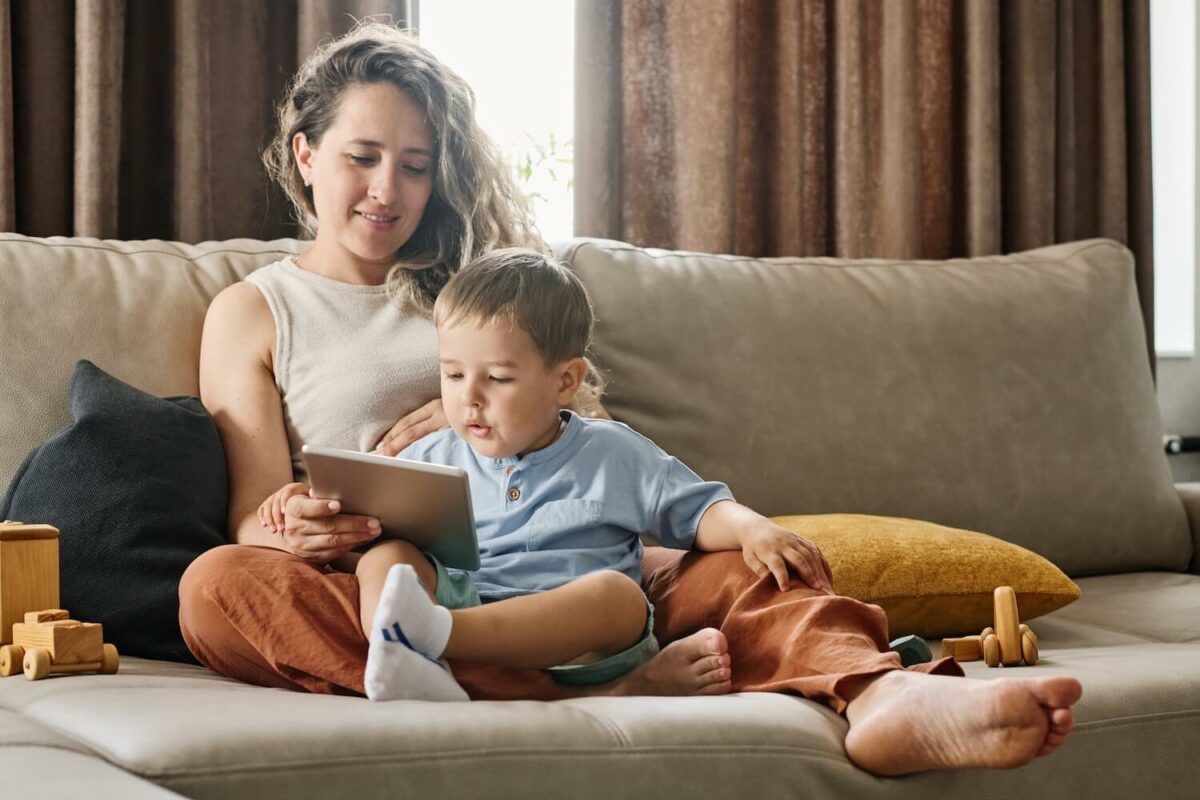 A mother and small child reading a book together on a couch